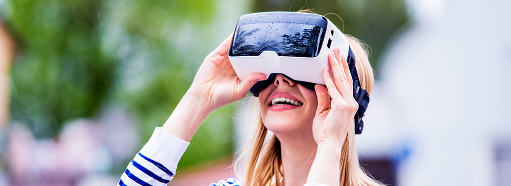 Blond woman in striped sweatshirt wearing virtual reality goggles in the street