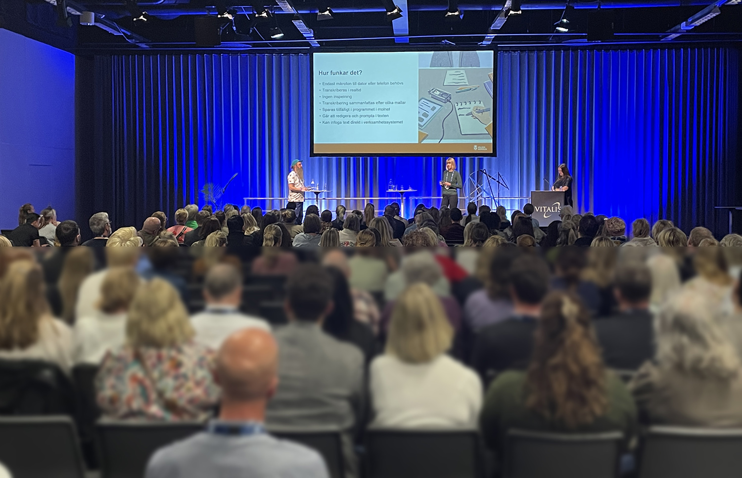 Publik framför en scen där tre personer talar